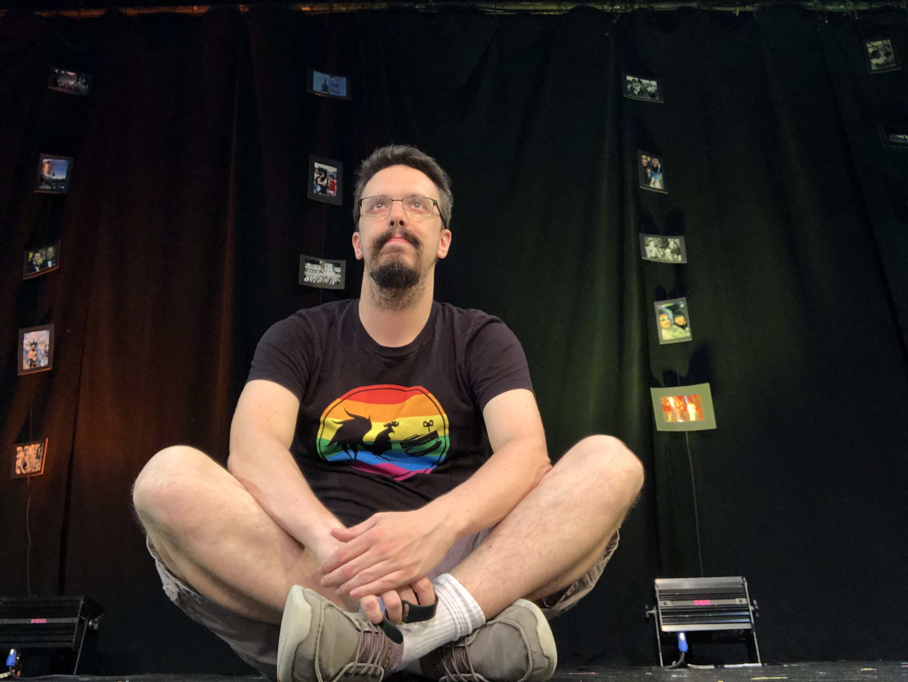 Riku sitting cross-legged on the set of Queer Shorts 2019, wearing a rainbow pride t-shirt.